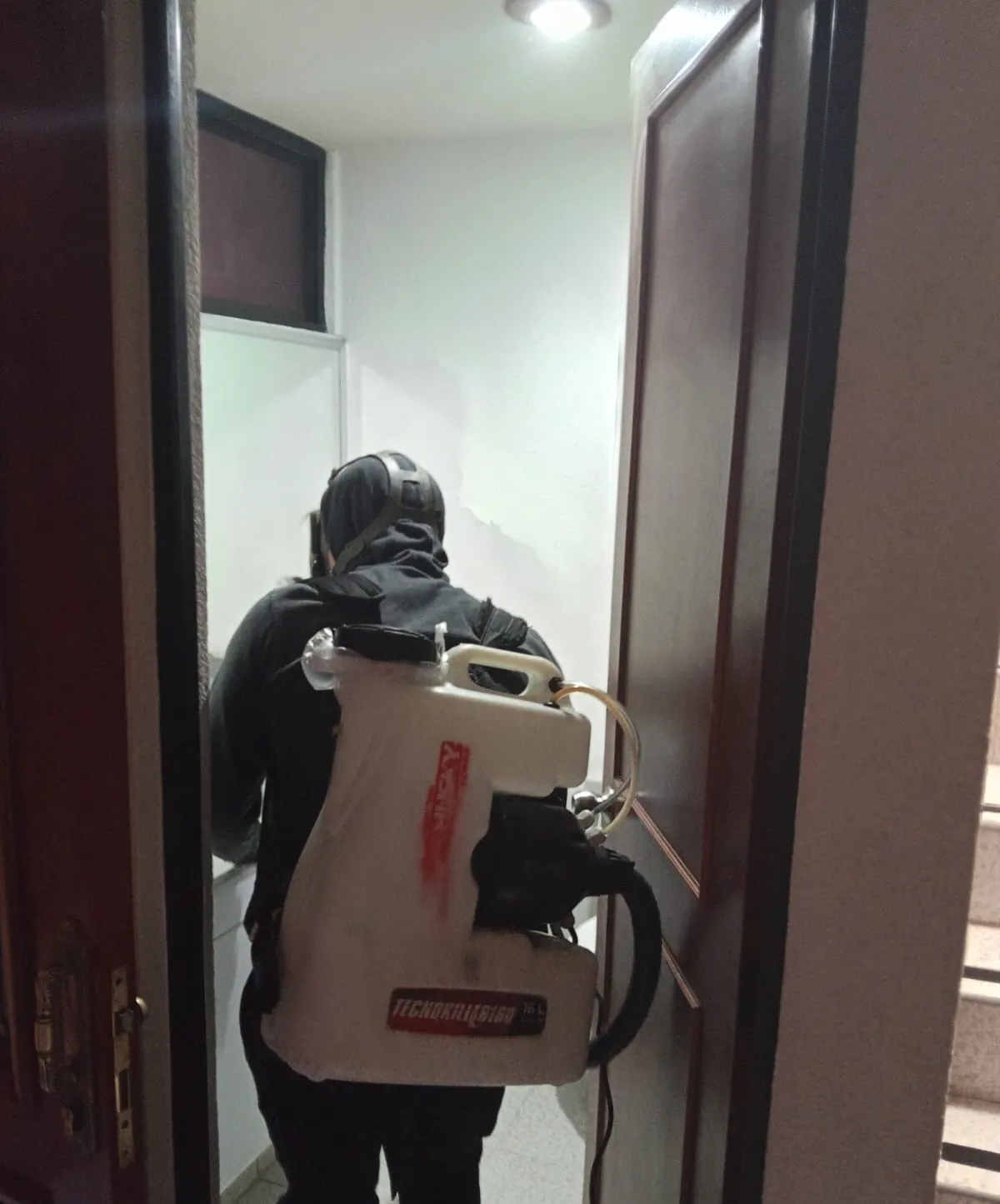 Un técnico en eliminación de plagas realizando un servicio para fumigar cucarachas dentro de un hogar.